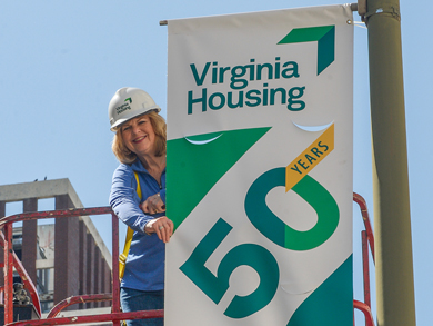 Susan Dewey, Virginia Housing CEO, hangs street banner celebrating 50 years of affordable housing