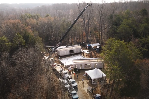 aerial shot of a crane dropping in modular home pieces on a cloudy day 