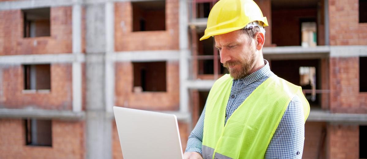 Construction worker reviewing plans on a laptop in an active apartment site